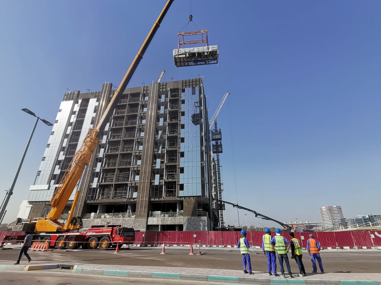 A crane lifting rooftop plant beside the Al Zebaq Property Airport Road Building during installation